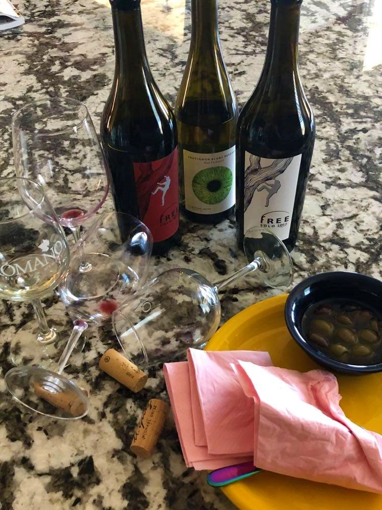 Empty wine glasses, a plate ready for the wash, a partially consumed bowl of olives and three partially consumed wine bottles.