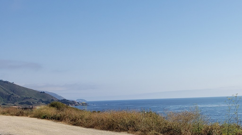 dirt pull out in foreground, ocean scene beyond the roadway