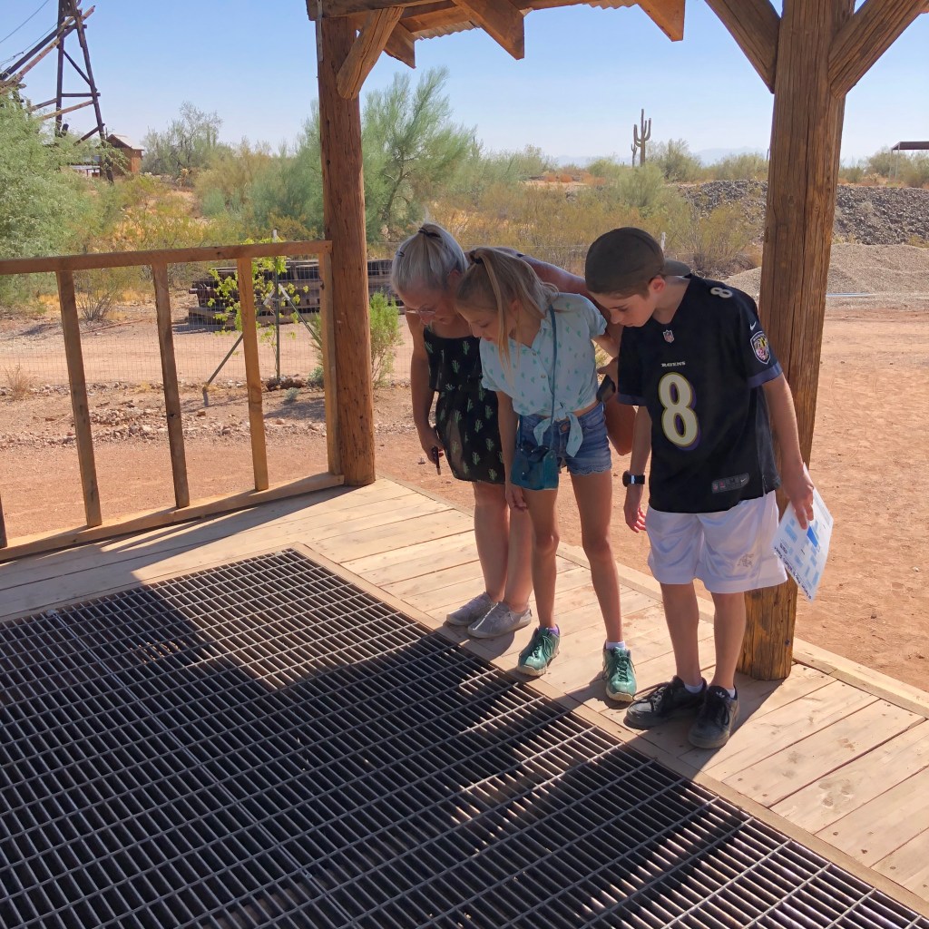 three people lean over abandoned mine shaft